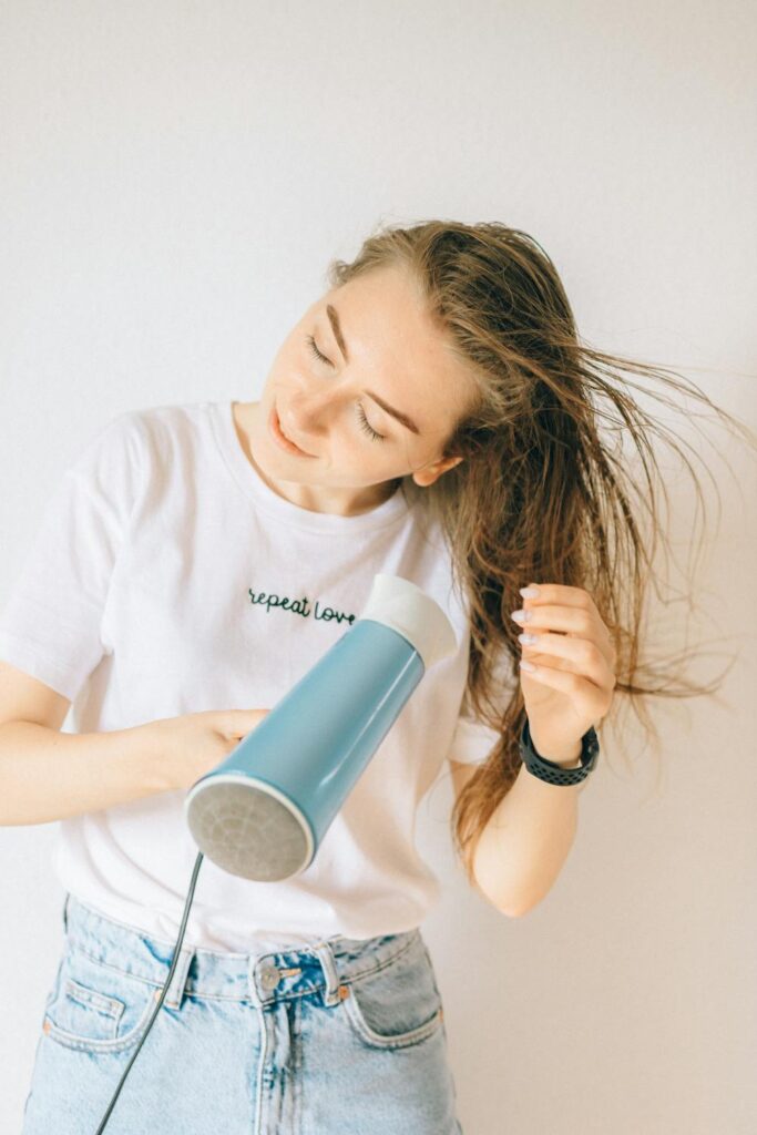 Woman using a blow dryer to lift roots and create fuller-looking hair at home
