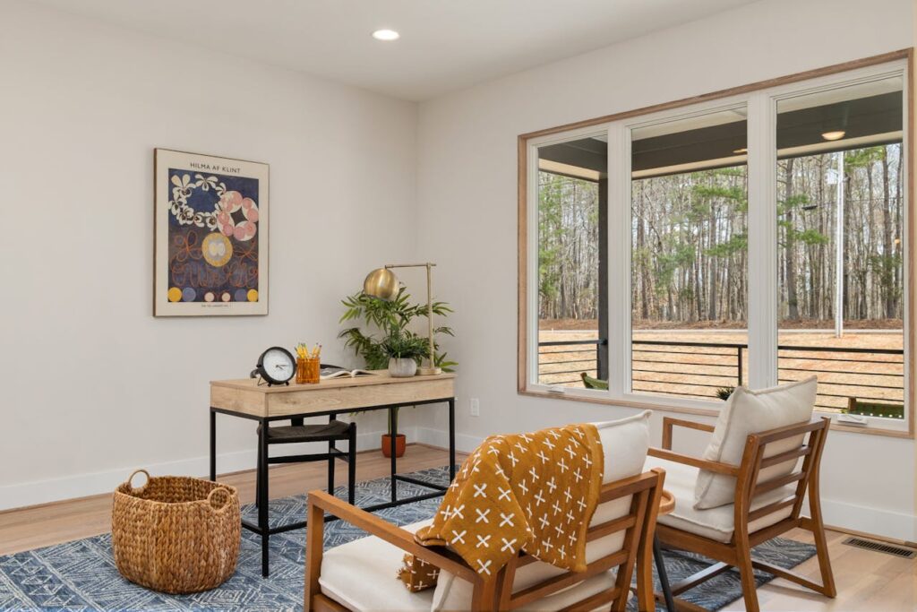 Cozy workspace with wooden desk, accent chairs, and large windows for natural light