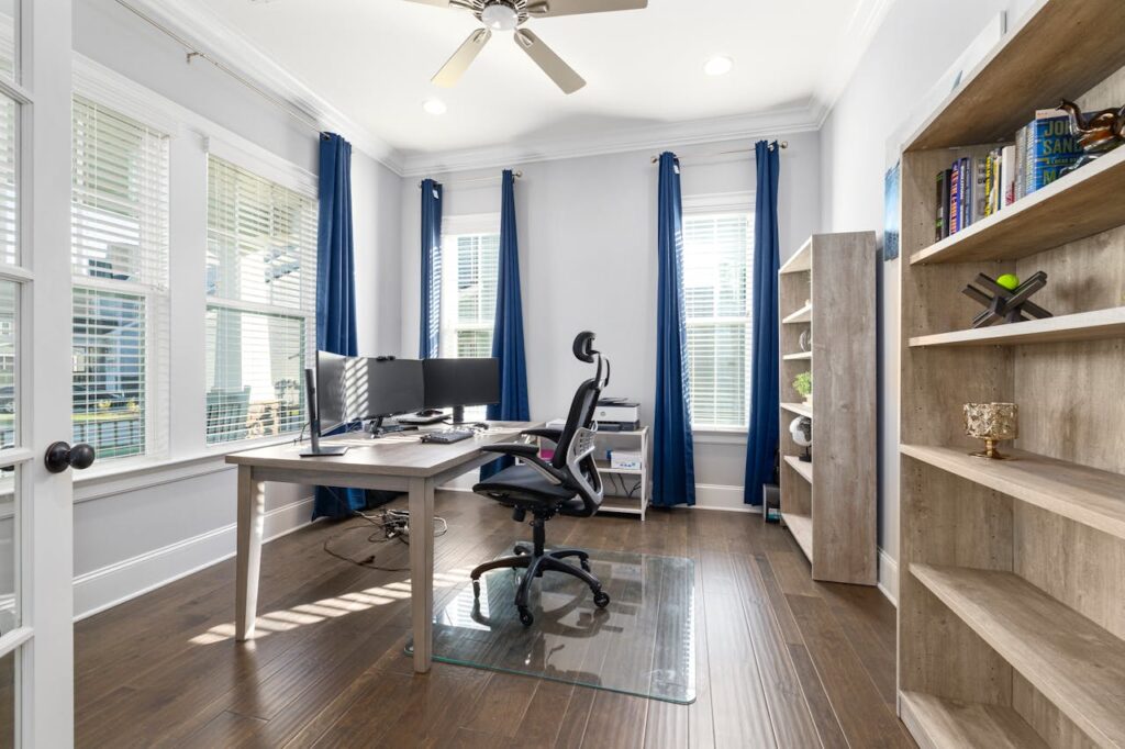 Modern home office with desk, dual monitors, and natural light from large windows