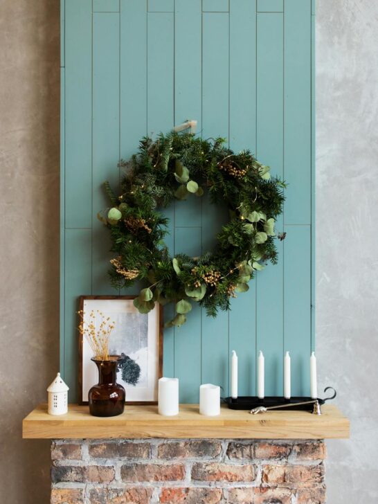 Decorated mantel with greenery wreath, candles, and framed art creating a warm and seasonal focal point