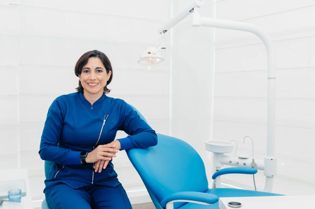 Female dentist sitting in a clean, modern dental office next to a treatment chair and equipment