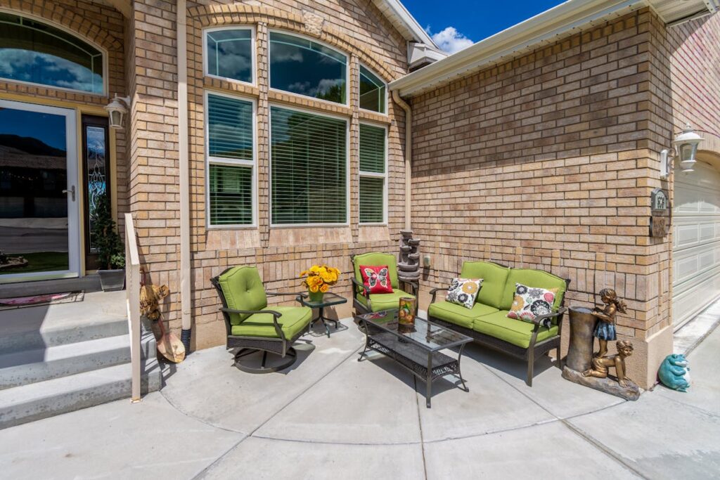 Outdoor seating area with green cushioned chairs and a glass table on a front patio
