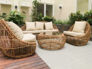 Wicker patio furniture set with cushions arranged around a round table in a garden-style courtyard