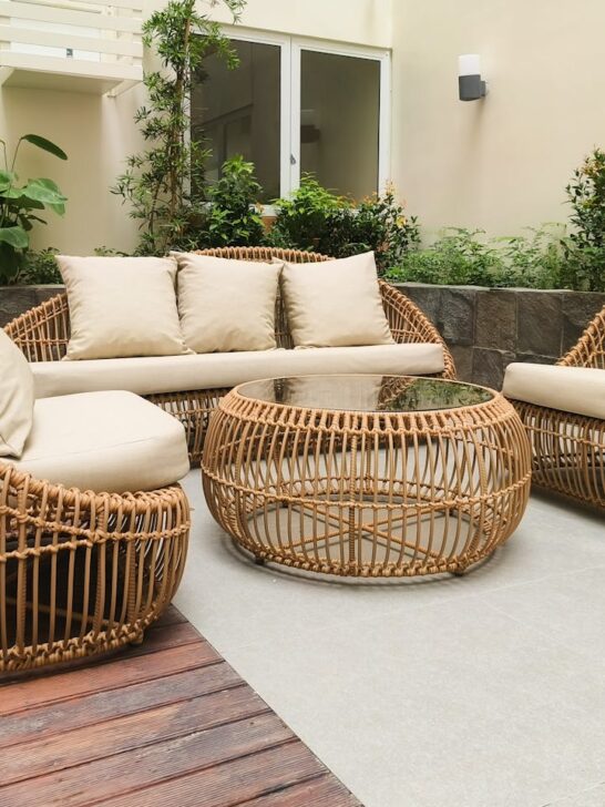 Wicker patio furniture set with cushions arranged around a round table in a garden-style courtyard