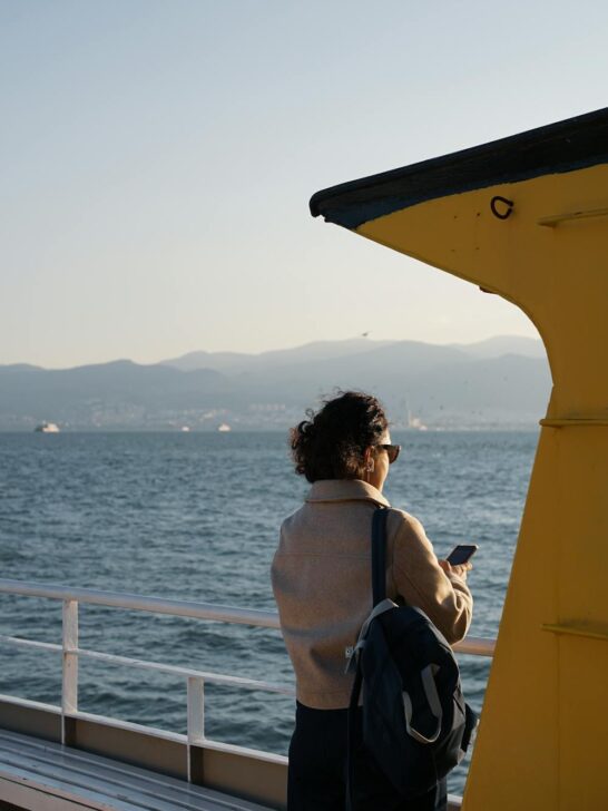 Woman traveling by ferry looking at her phone with water and mountains in the background