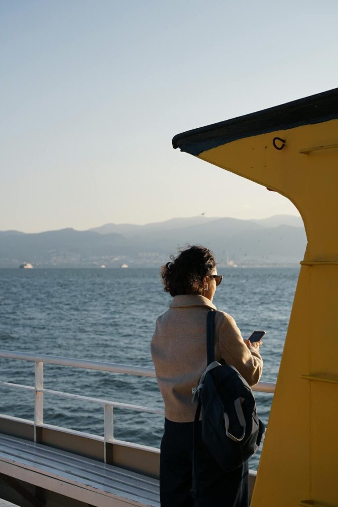 Woman traveling by ferry looking at her phone with water and mountains in the background
