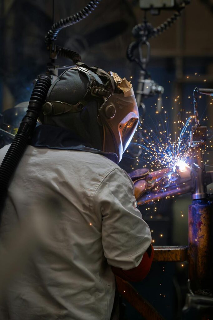 Welder using pipeliner welding helmets while working on metal pipe with sparks flying in a workshop