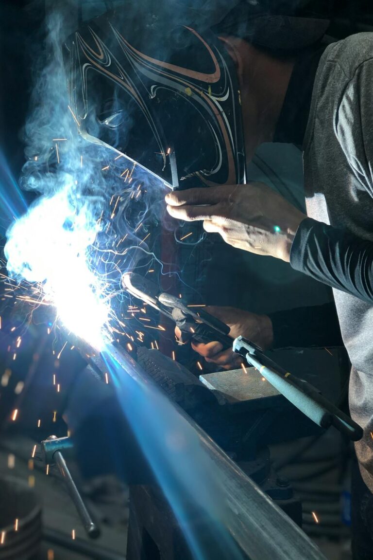 Close-up of welder using torch on metal pipe with bright sparks and protective helmet in a dim workspace