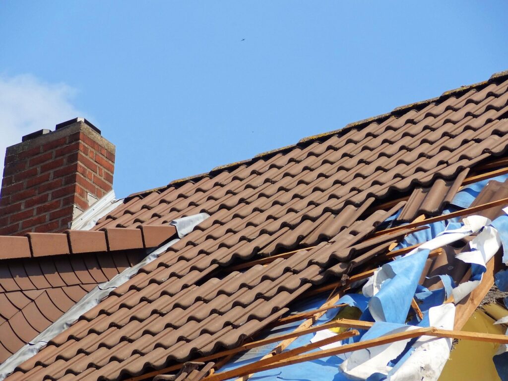 Roof with visible storm damage including broken tiles and exposed interior layers near chimney


