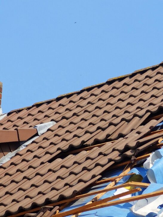 Roof with visible storm damage including broken tiles and exposed interior layers near chimney