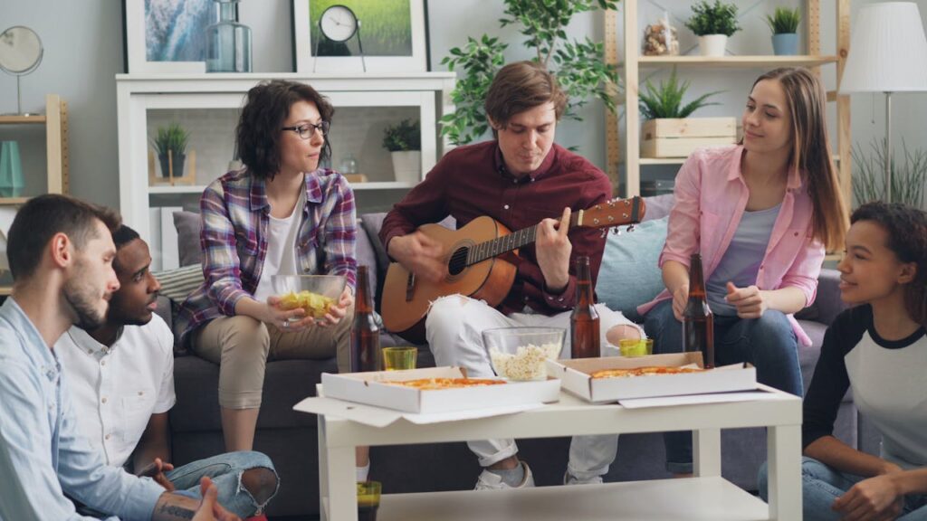 Friends gathered in a living room eating pizza and playing guitar during a relaxed get-together