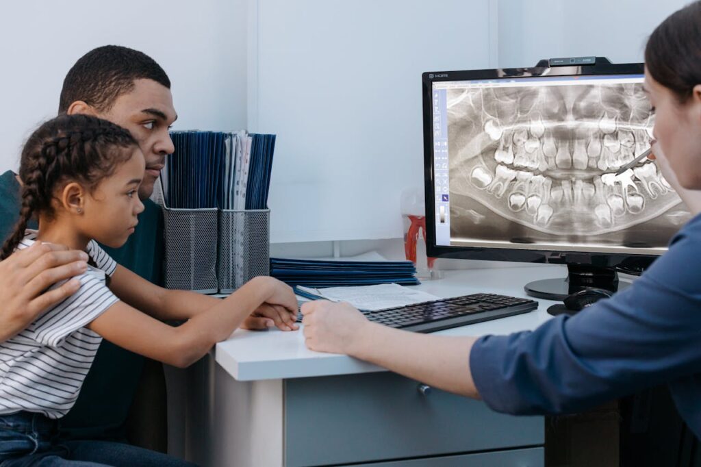 Dentist showing dental X-ray to parent and child during consultation for wisdom tooth extraction treatment