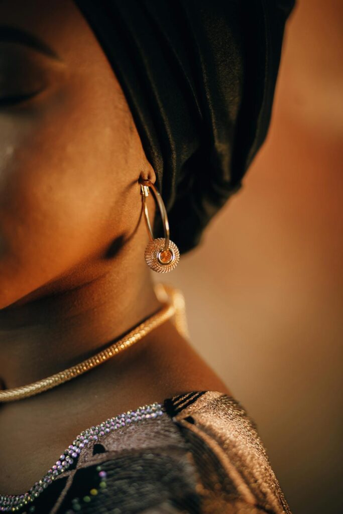 Close-up of gold hoop earring with textured charm paired with layered jewelry and dark outfit