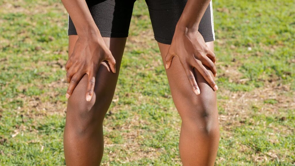 Person holding both knees while standing outdoors, showing discomfort from knee pain during activity