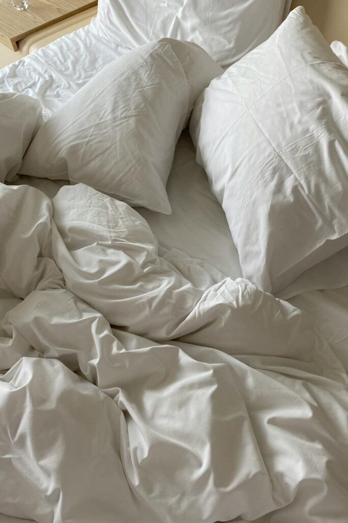 Crisp white bedding and pillows arranged on a bed showing how to sleep better at night with a clean, comfortable setup