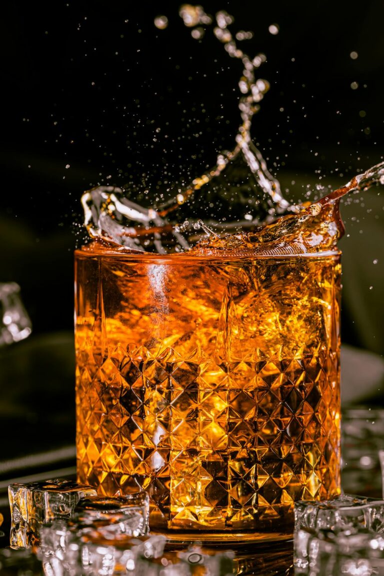 Whiskey collection splash in crystal glass with ice cubes and dramatic amber lighting creating a bold, luxurious cocktail moment.