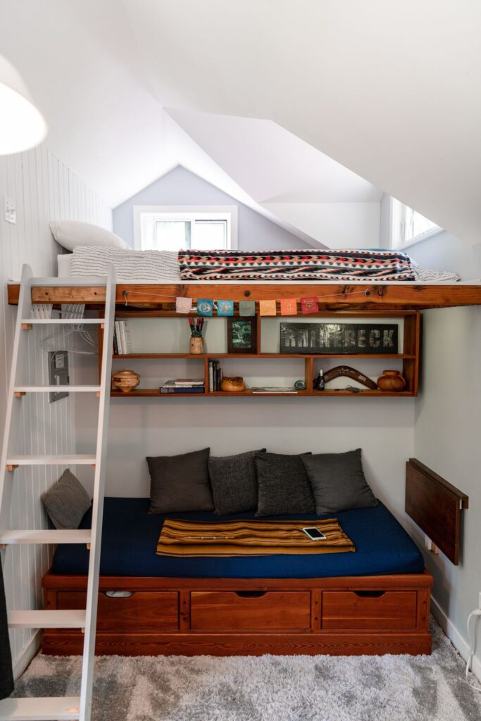 Small bedroom with a loft bed, built-in shelving, storage drawers, and a space-saving layout designed to maximize floor space and functionality.