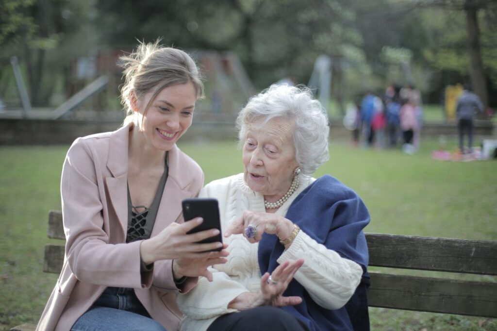 An older woman and caregiver reviewing location and safety information on a smartphone while spending time together outdoors.