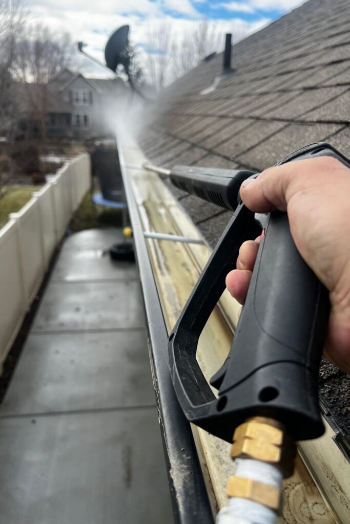 Homeowner pressure washing gutters and roof edges to remove buildup, improve drainage, and maintain a clean, well-kept exterior.