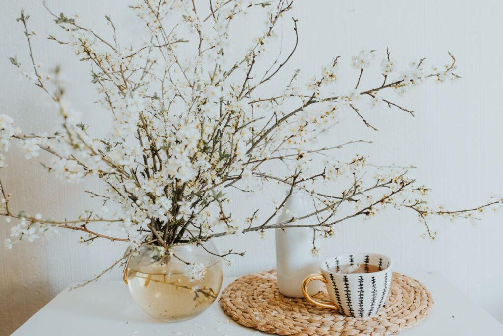 Spring home decor ideas featuring delicate white flowering branches displayed in a glass vase on a bright table with woven placemats and neutral decor accents.
