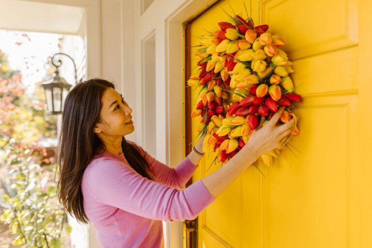Woman hanging a colorful tulip wreath on a bright yellow front door as part of a simple spring home decor refresh.