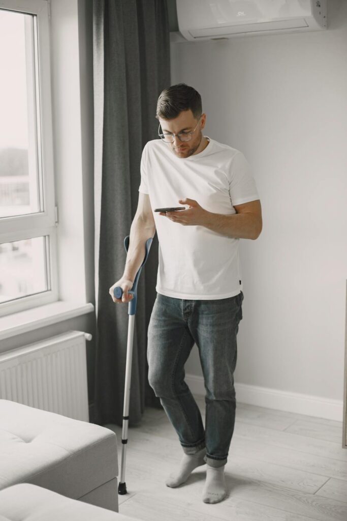 Person using a crutch while checking a smartphone during recovery from delayed injury symptoms after a car accident.