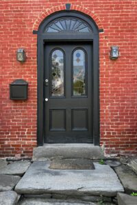 Black arched front door with decorative glass panels set in a historic red brick exterior wall
