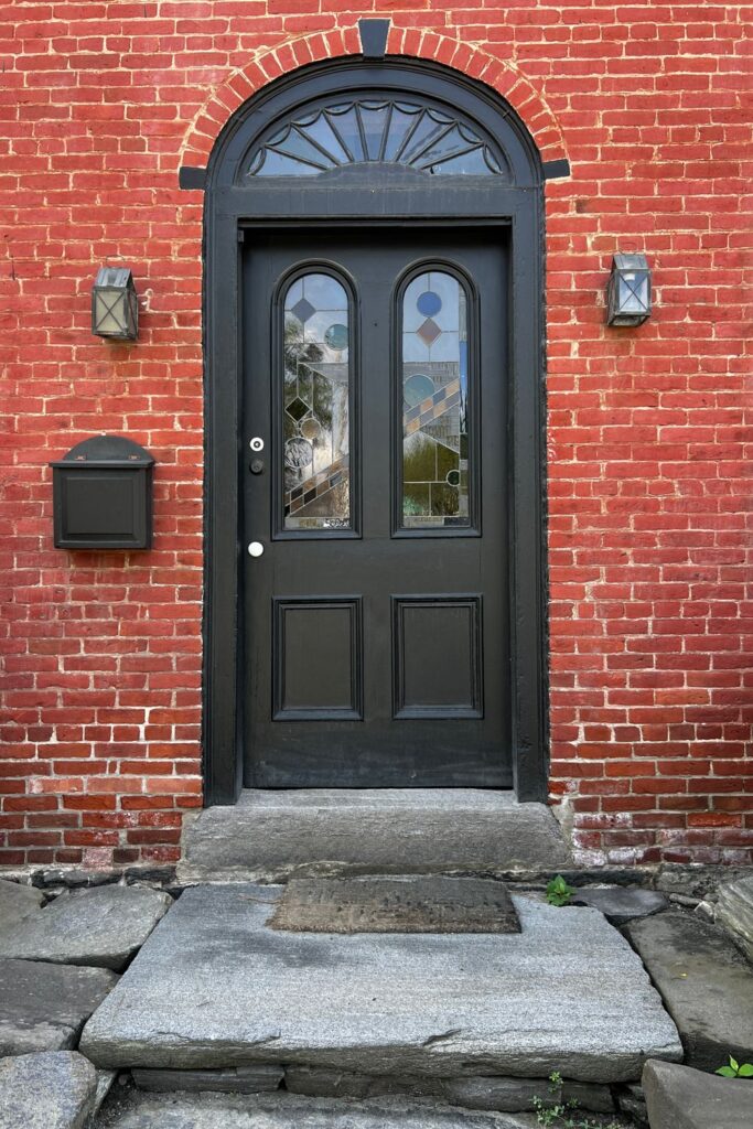 Black arched front door with decorative glass panels set in a historic red brick exterior wall