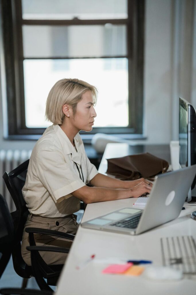 Person sitting at a desk with proper posture while working on a laptop, demonstrating habits that may help improve facial symmetry without surgery.