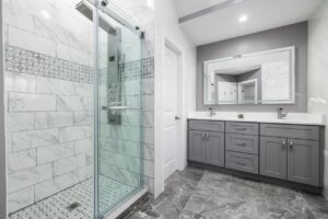 Modern bathroom featuring smart shower technology, marble-look tile walls, glass shower enclosure, and gray double vanity.