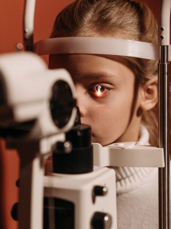 Child undergoing a children's vision check with a slit lamp eye exam machine during a routine pediatric eye appointment.