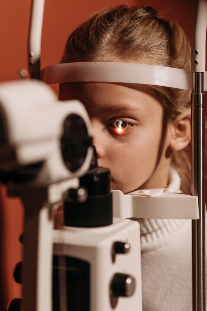 Child undergoing a children's vision check with a slit lamp eye exam machine during a routine pediatric eye appointment.