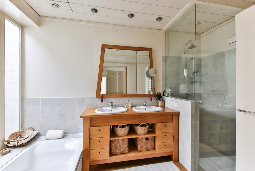 Bright bathroom with a double vanity, wood cabinetry, dual sinks, woven storage baskets, a glass walk-in shower, and a soaking tub, offering practical Bathroom plumbing tips for homeowners planning a remodel.