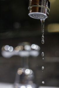 Close-up of a dripping bathroom faucet with water droplets falling from the aerator, highlighting a common plumbing issue that may require repair.