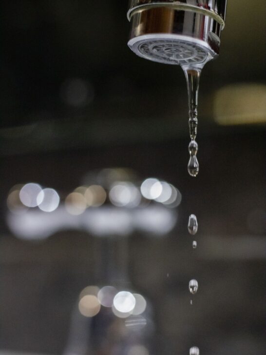 Close-up of a dripping bathroom faucet with water droplets falling from the aerator, highlighting a common plumbing issue that may require repair.