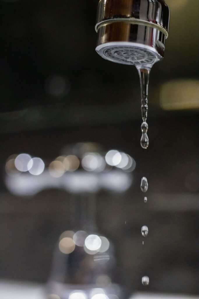Close-up of a dripping bathroom faucet with water droplets falling from the aerator, highlighting a common plumbing issue that may require repair.