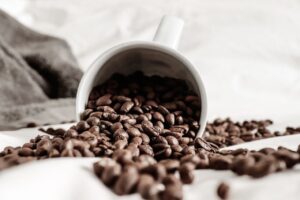 How to store coffee beans for maximum freshness with whole roasted coffee beans spilling from a white mug.