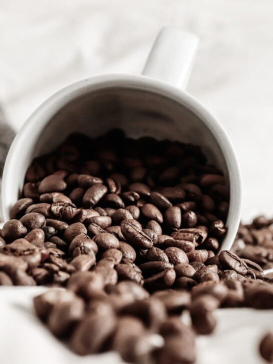 How to store coffee beans for maximum freshness with whole roasted coffee beans spilling from a white mug.