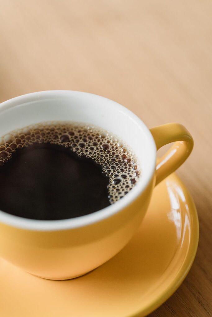 Freshly brewed black coffee served in a yellow coffee cup on a wooden table.