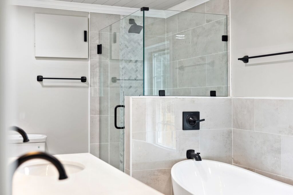 Modern bathroom with a freestanding tub, glass shower enclosure, black fixtures, and large neutral wall tiles.