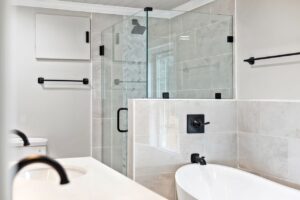 Modern bathroom with a freestanding tub, glass shower enclosure, black fixtures, and large neutral wall tiles.