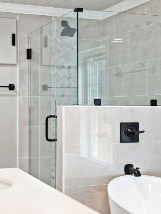 Modern bathroom with a freestanding tub, glass shower enclosure, black fixtures, and large neutral wall tiles.