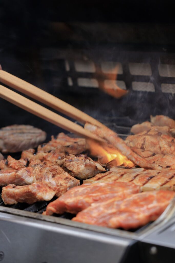 Charcoal vs gas grills comparison showing a gas grill cooking chicken, pork, and burgers over high heat for an easy backyard barbecue.