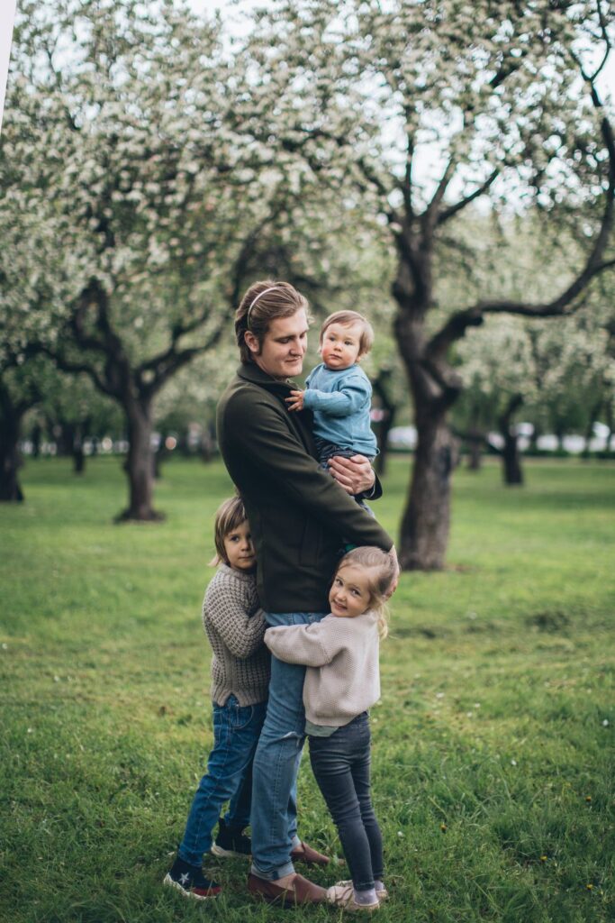 Parent spending quality time outdoors with three young children in a park.