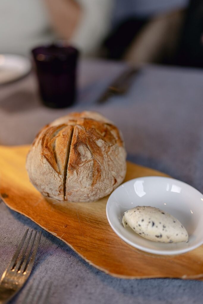 Rustic loaf of bread served with a scoop of homemade herb butter on a wooden board.
