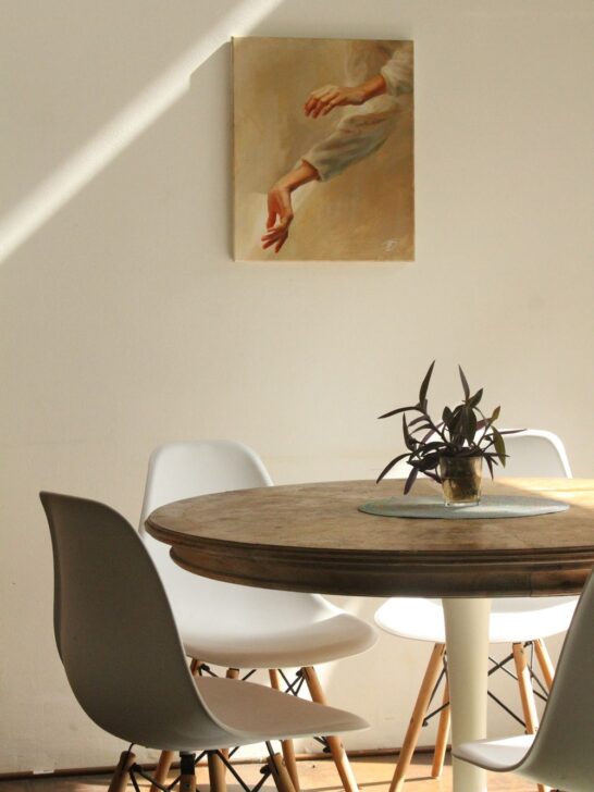 Round wooden dining table with white chairs in a bright dining room, creating a comfortable and inviting space for everyday meals.