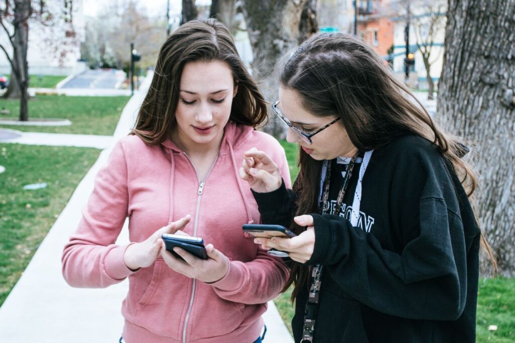 Teenagers looking at their smartphones together outdoors while checking messages and social media.