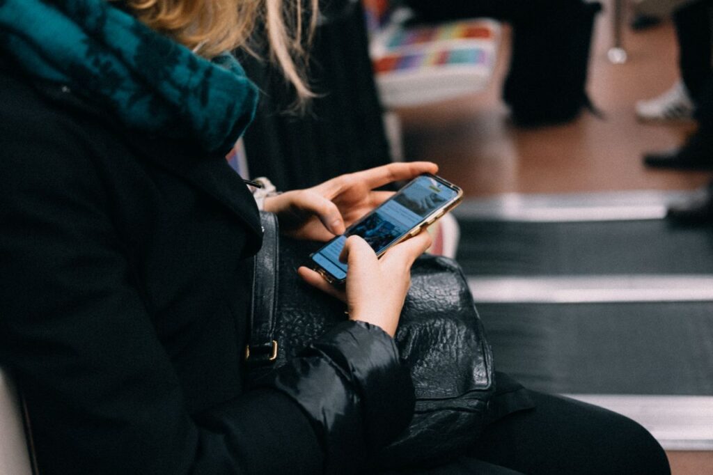 Woman using a smartphone while sitting in a public space, showing everyday mobile phone use and digital distractions.