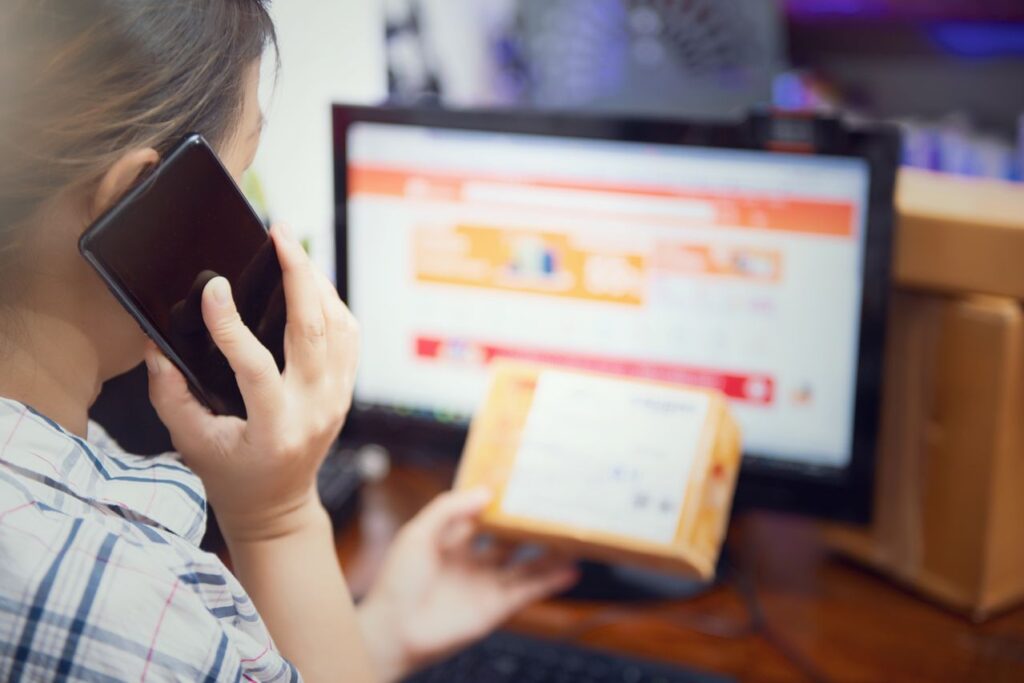 Business owner speaking on the phone while processing an online order and preparing a package for shipment.