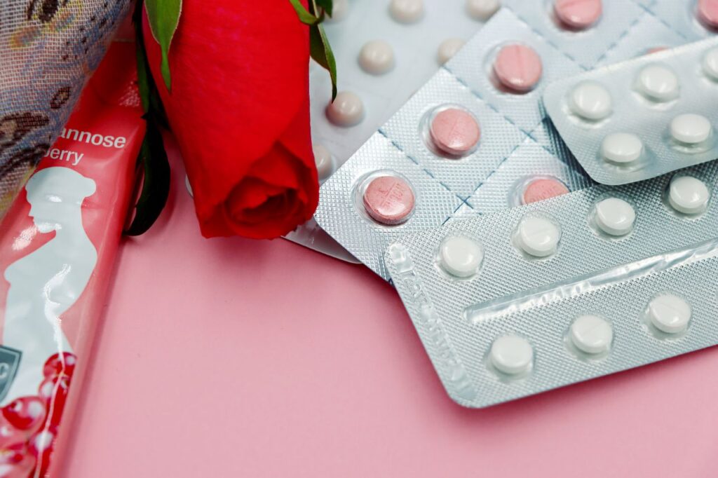 Birth control pill packs with a red rose on a pink background.
